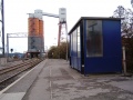 The station and platform shelter are somewhat dwarfed by the industrial equipment that surrounds them.